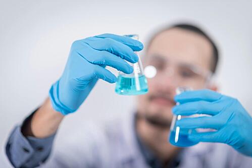 A man wearing blue gloves, inspecting some test tubes that contain blue liquid